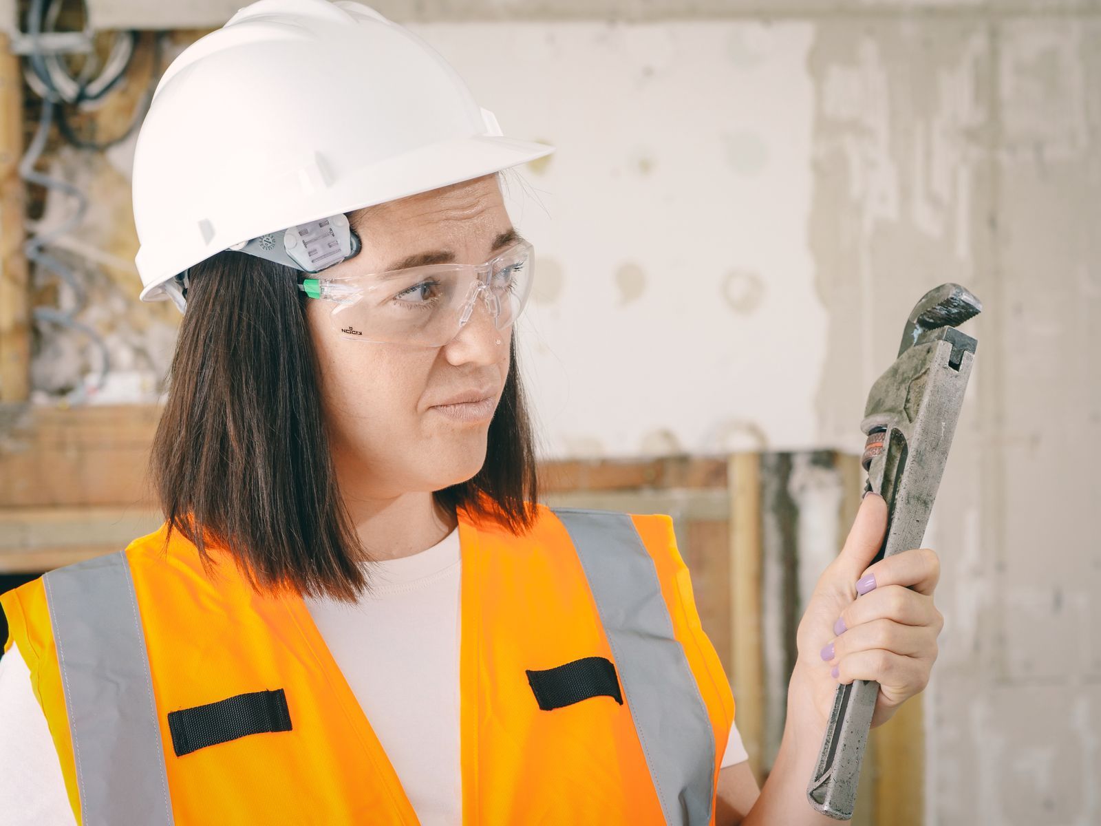 Monteurin mit Schutzhelm und Rohrzange auf einer Baustelle